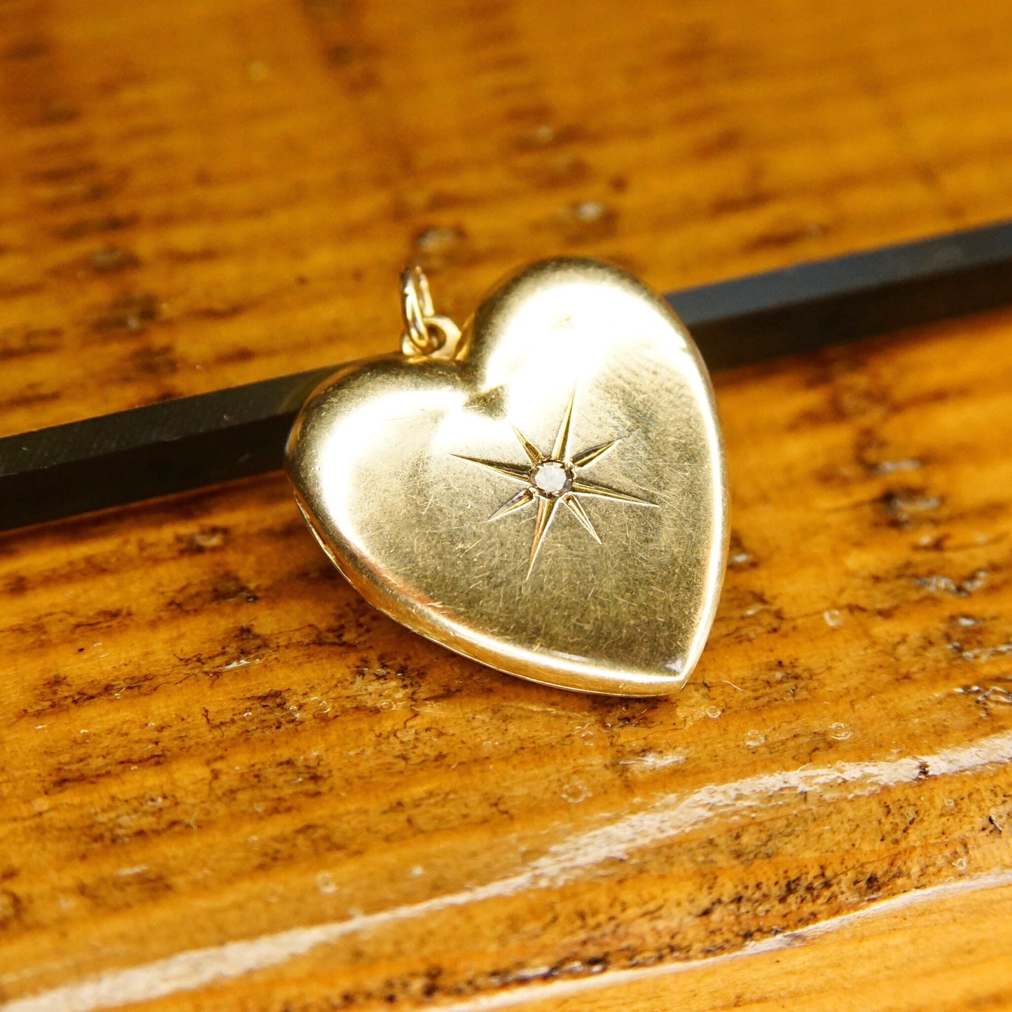 Antique 14K gold heart locket with diamond starburst design on wooden surface