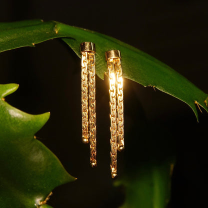 Vintage 14K gold tassel earrings with two strands of anchor link chains hanging from leaves, set against a dark background.