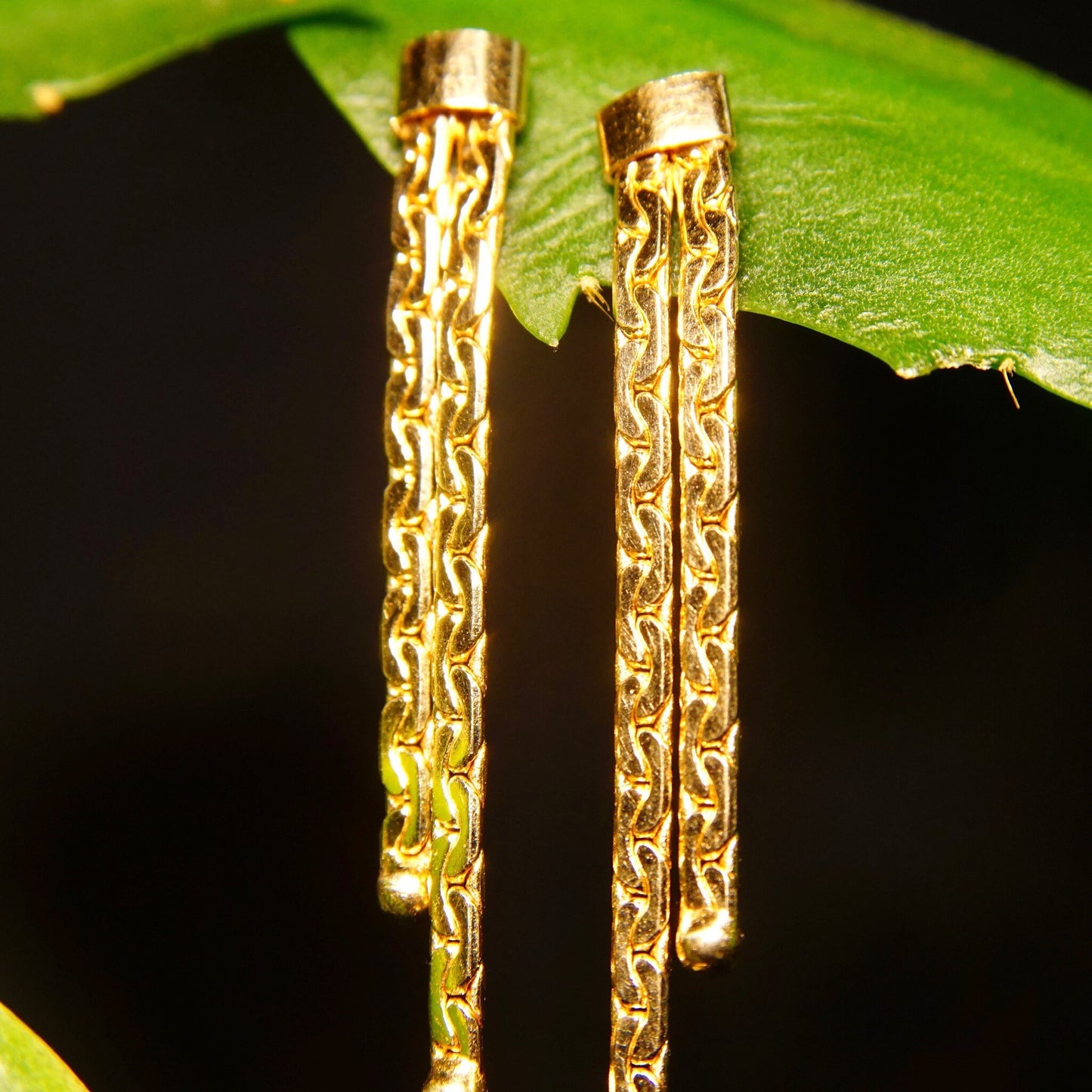 Vintage 14K gold chain tassel dangle earrings with push backs, featuring two strands of intricately linked half anchor chains, measuring approximately 1 3/8 inches in length against a green leaf background.