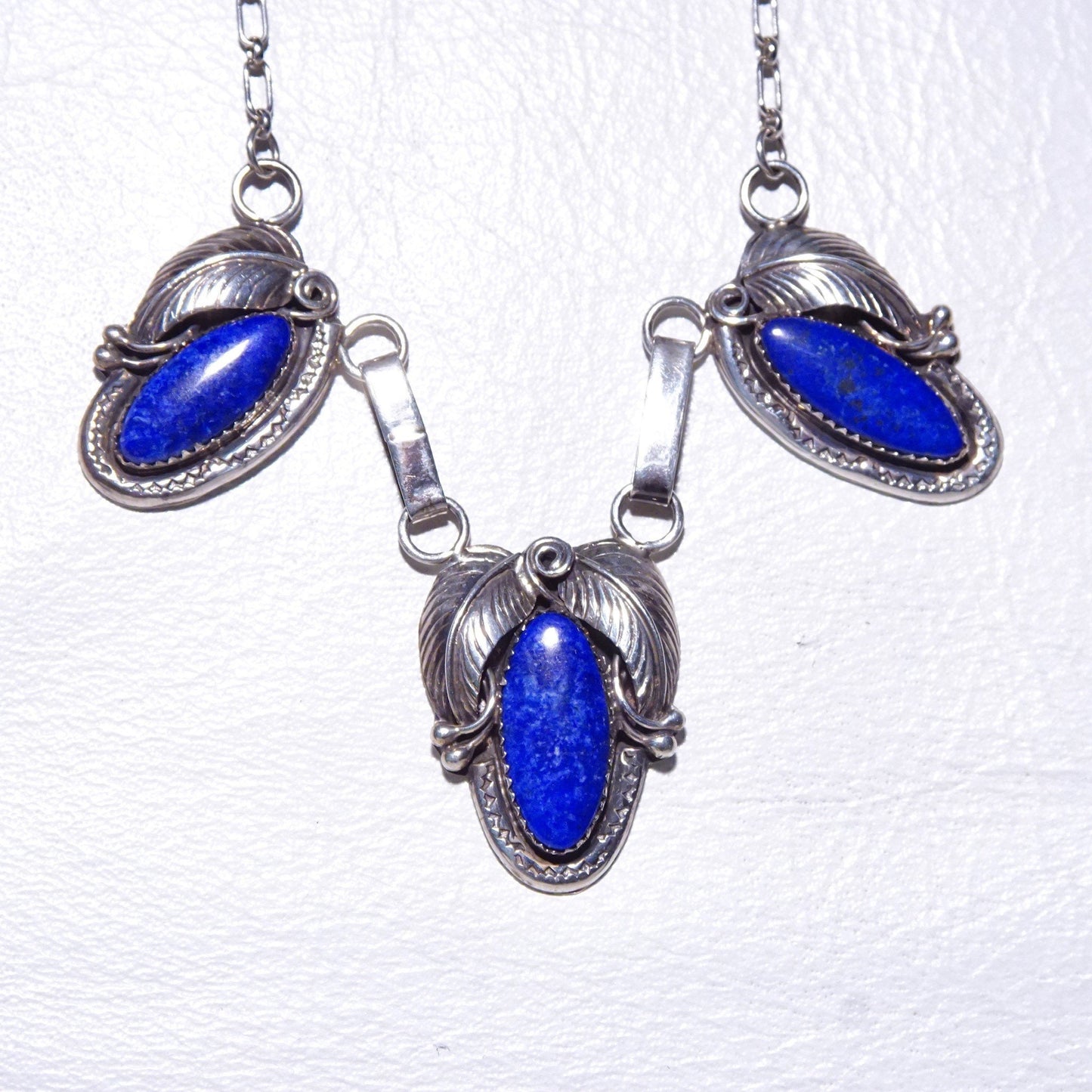 Vintage Native American sterling silver necklace featuring a three-stone pendant with oval lapis lazuli cabochons set in intricately engraved leaf settings, suspended from an oval link chain measuring 20 3/4 inches in length.