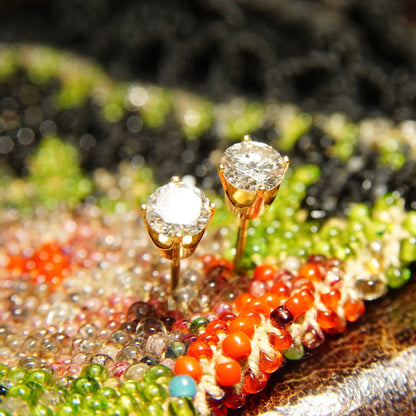 Colorful bead embroidery featuring rows of green, orange, red and clear beads with two round-cut diamonds set in gold studs prominently displayed on top of the embroidered surface, suggesting vintage or antique diamond stud earrings on an intricate beaded background.