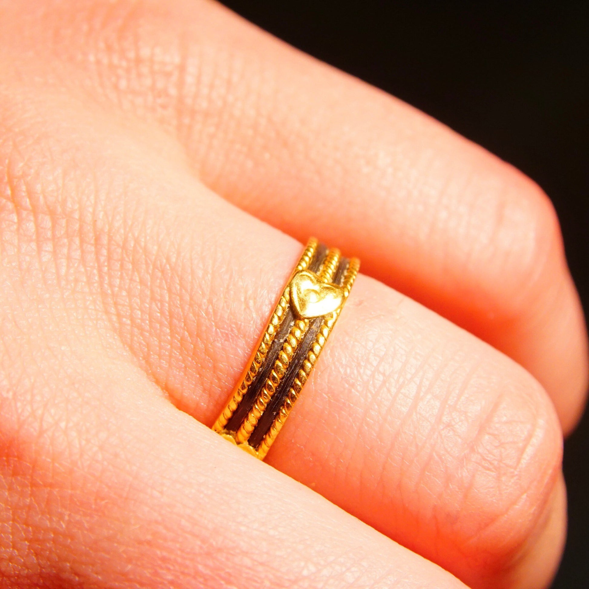 Vintage 22K yellow gold wedding band with black enamel inlay and heart embellishments, handmade Indian jewelry, shown on a finger.