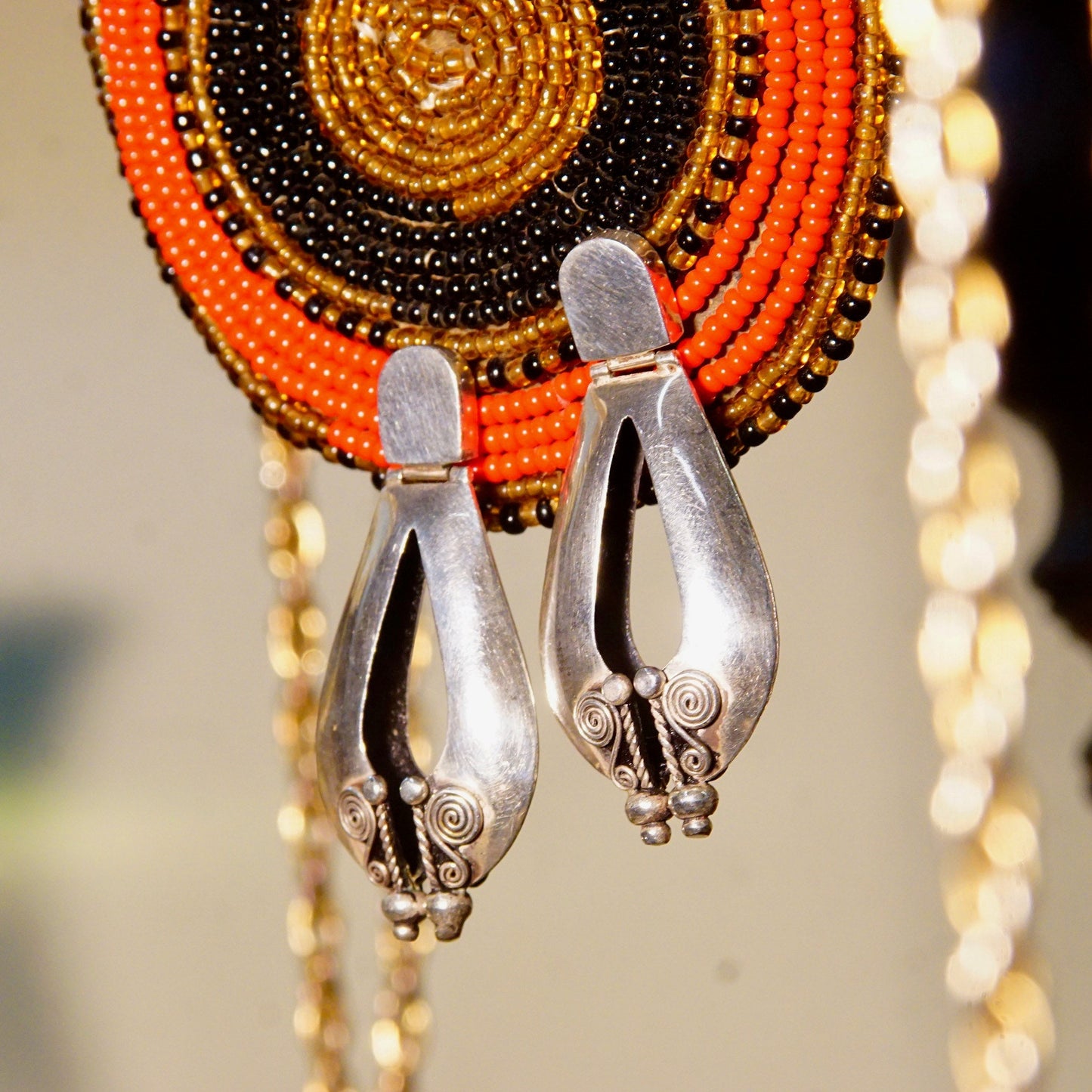 Vintage Bali style sterling silver pierced dangle earrings with puffed teardrop design and wire wrap details, featuring intricate orange, red and black beaded necklaces in the background, measuring 1 7/8 inches long, 925 Boho accessories.