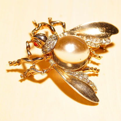 Golden vintage brooch featuring a fly design with a pearl-like body, clear and red rhinestone details, and gilt silver wings, crafted by Trifari in the Alfred Philippe style.