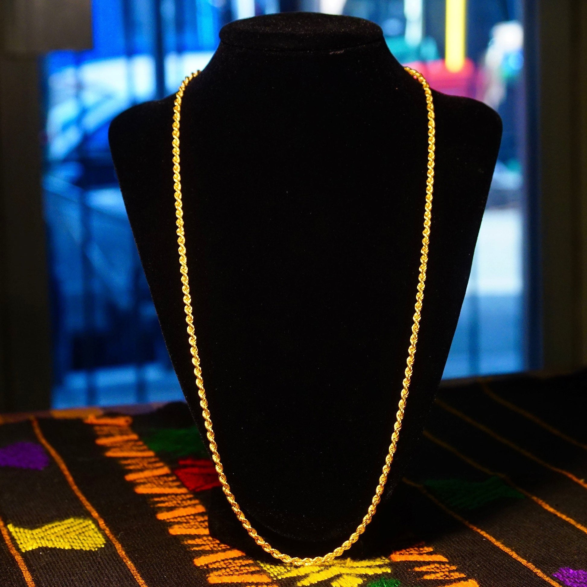 14K yellow gold vintage hollow rope chain necklace displayed on black velvet with colorful geometric patterned fabric underneath