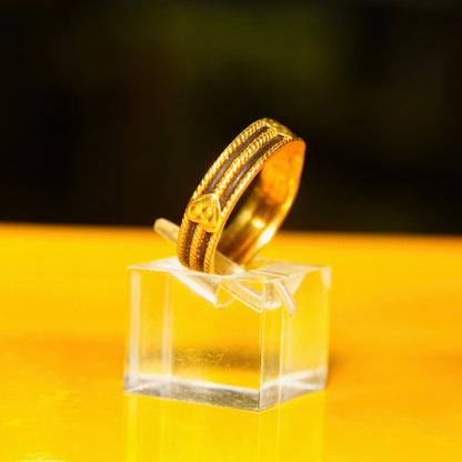 Vintage 22KT yellow gold wedding band with black inlay and gold heart embellishments on display stand against yellow background