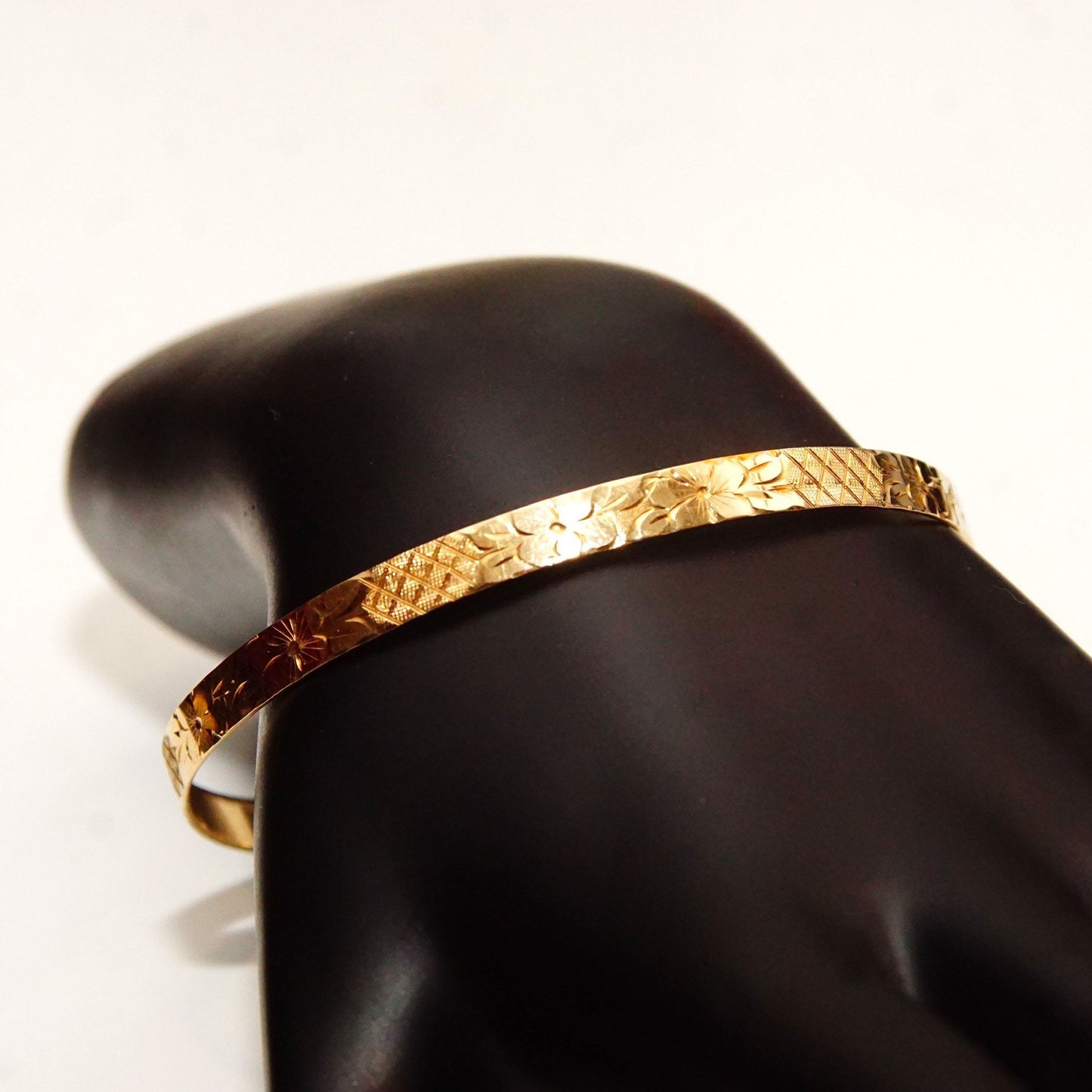 14K solid yellow gold bangle bracelet with floral motifs and diamond-cut designs, 5mm wide, perfect for stacking, shown on dark jewelry display hand.