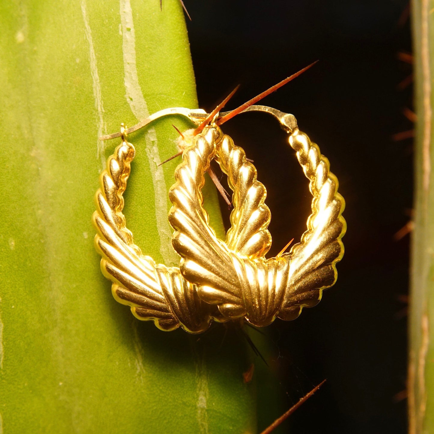 Vintage 14K yellow gold scalloped hoop earrings in a puffed wreath design, measuring 1 1/4 inches long, resting on a green leaf.