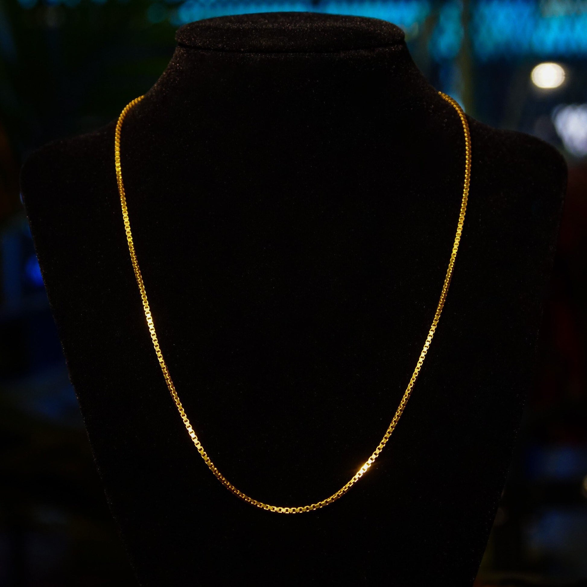 Vintage Italian 14K solid yellow gold box chains, 1.5mm thin, fine pendant necklace chains in 16 and 18 inch lengths, displayed on black velvet jeweler's bust in dim lighting with blue background bokeh.