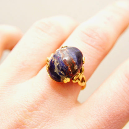 Vintage 10K gold-filled lapis lazuli cabochon ring with dark blue gemstone showing golden inclusions, set in a yellow gold ribbon-embellished setting, on a hand to show scale, ring size 8 US.