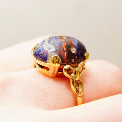 Vintage 10K yellow gold filled ring featuring a dark blue lapis lazuli cabochon with golden inclusions, accented by ribbon-like gold embellishments on the band, photographed on a hand to show scale, size 8 US ring.