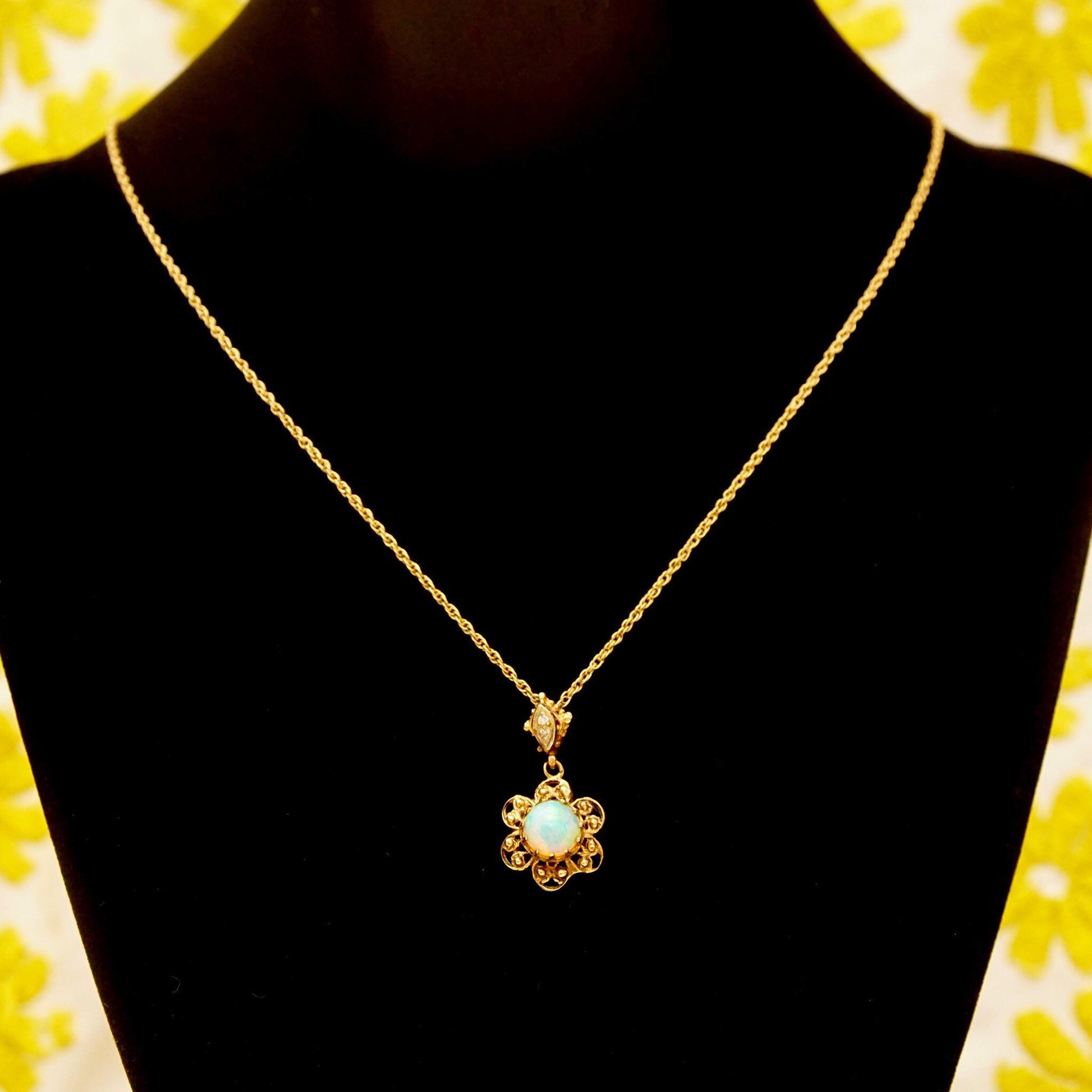 14K gold filigree opal flower pendant necklace with diamond accents on loose rope chain against floral background