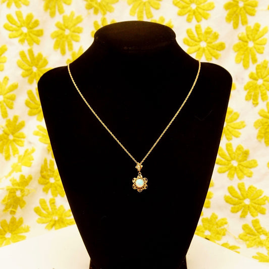 14K gold filigree opal flower pendant necklace with diamond accents on black velvet display with yellow floral background