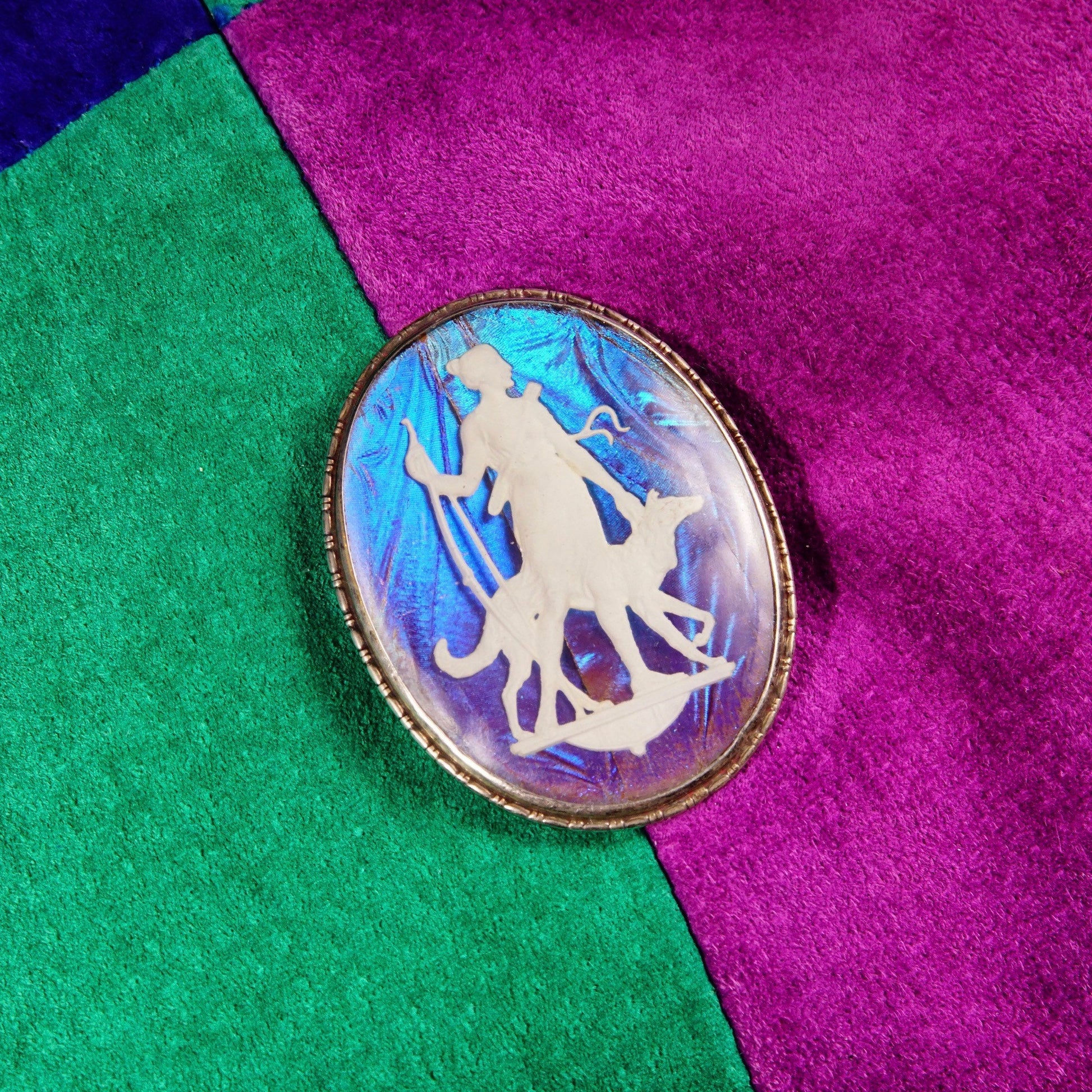 Vintage Art Deco sterling silver butterfly wing cameo brooch pin featuring an iridescent sulfide cameo depicting a Grecian goddess, made in England, measuring 1 3/4 inches long, set against a background of purple and green felt or velvet fabric.