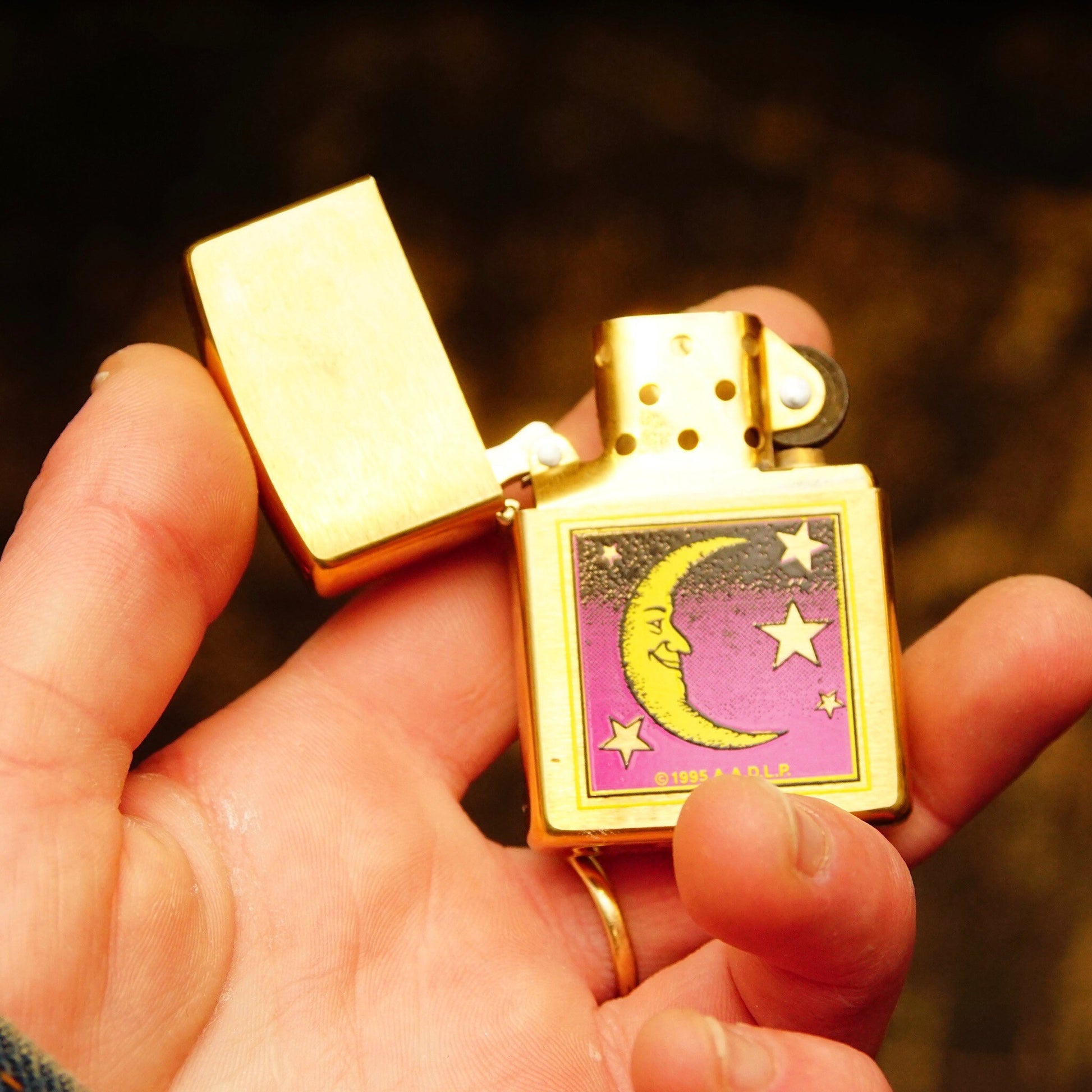 Vintage 1995 AADLP brass Zippo lighter featuring a decorative crescent moon and stars design, held in a person's hand, measuring 2 1/4 inches in size, made in Bradford, PA, USA.