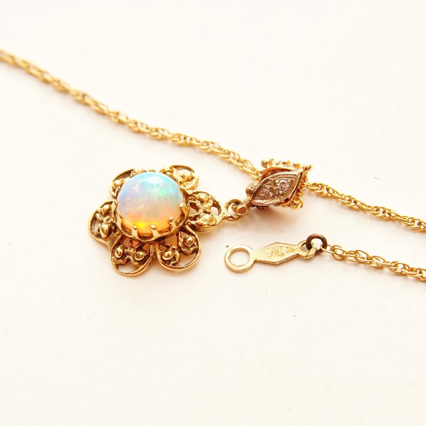 14K gold filigree flower pendant necklace with opal cabochon center stone and diamond accents on bail, featuring delicate 1.5mm rope chain, 21 inches long.