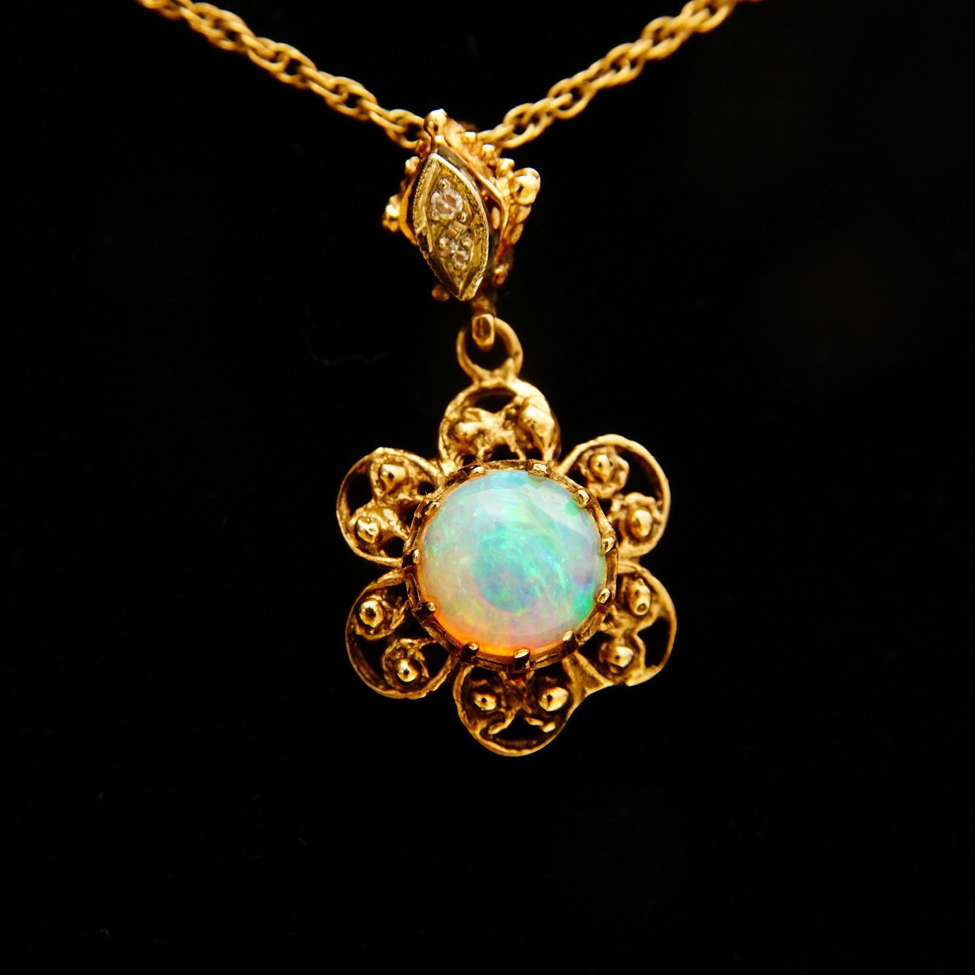14K gold filigree flower pendant necklace featuring an iridescent opal cabochon center stone accented by two small diamonds, suspended from a delicate 1.5mm rope chain measuring 21 inches in length.