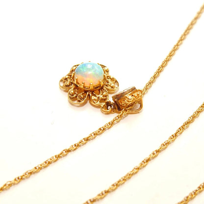 14K yellow gold filigree flower pendant featuring a round opal cabochon center stone accented by two small diamonds, suspended from a delicate 1.5mm rope chain necklace measuring 21 inches in length.