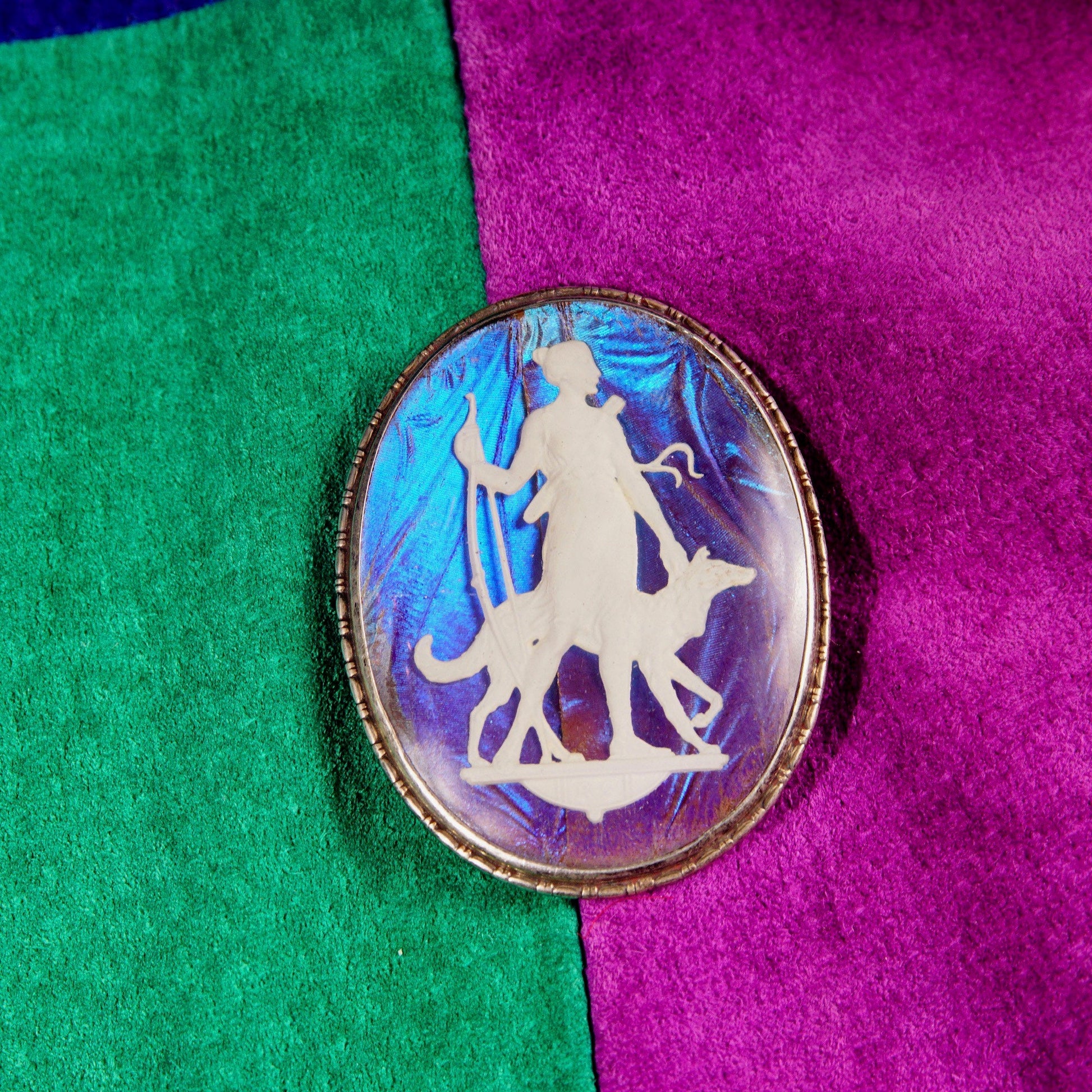 Vintage Art Deco Sterling Silver Butterfly Wing Cameo Brooch featuring an iridescent sulfide cameo depicting a Grecian goddess figure, made in England, measuring 1 3/4 inches long, set against a green and purple fabric background.