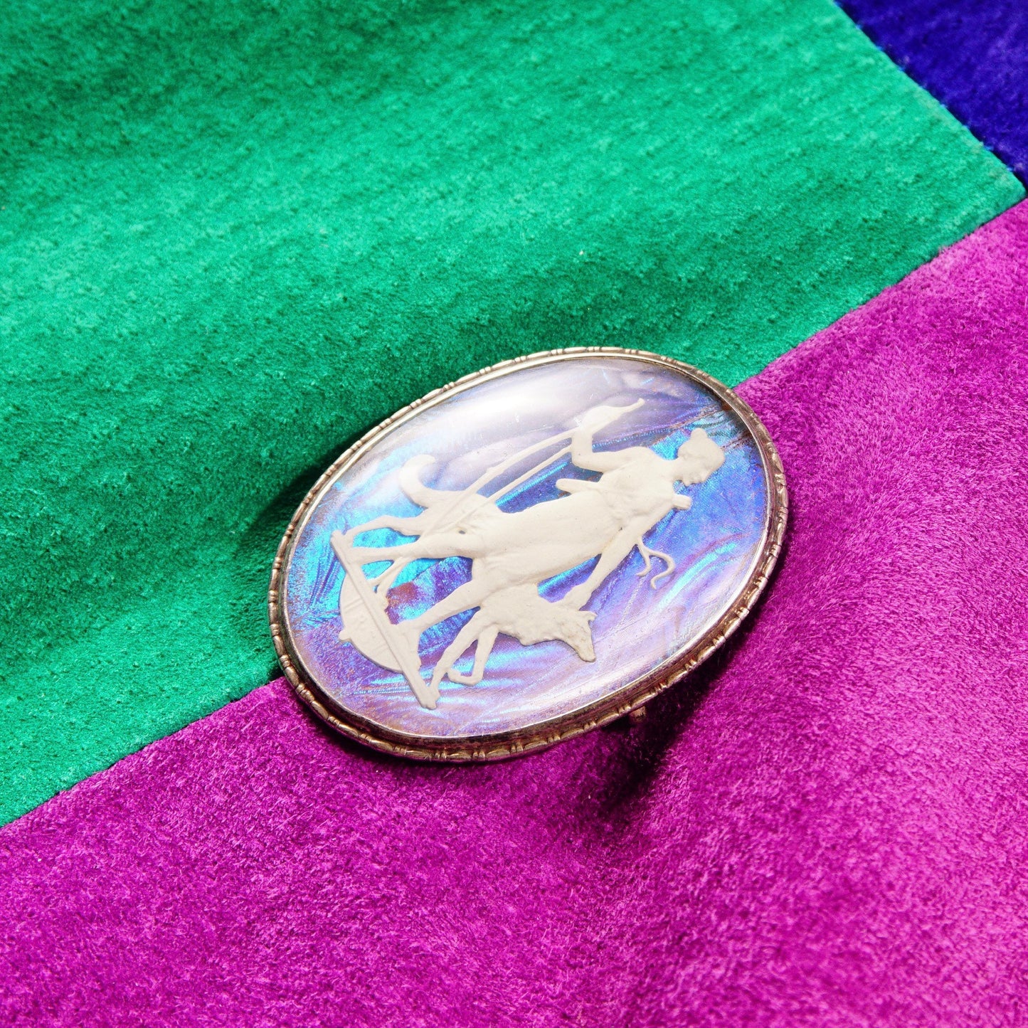 Vintage Art Deco sterling silver brooch featuring an iridescent butterfly wing sulfide cameo depicting a Grecian goddess, made in England, measuring 1 3/4 inches long, displayed on a colorful felted background in shades of green, blue and purple.