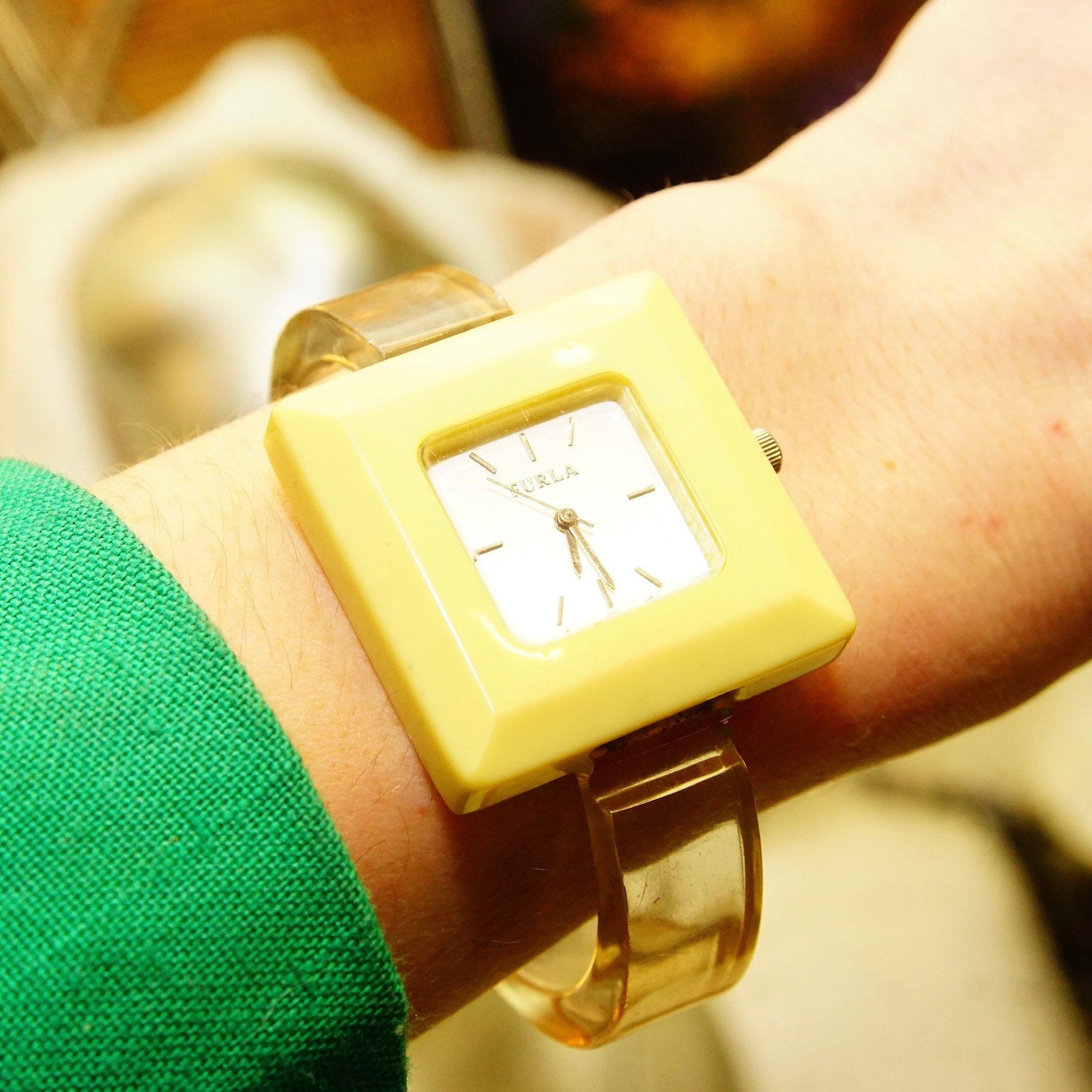 Vintage yellow plastic Furla cuff wristwatch with square case and reflective white dial on a person's wrist wearing a green shirt