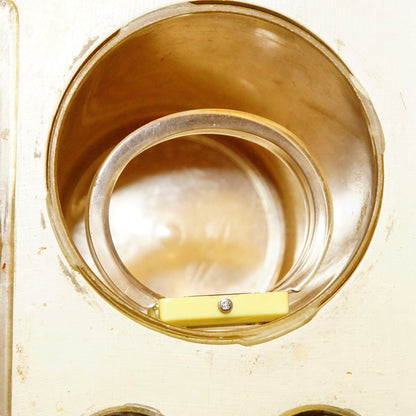 Vintage gold-toned cuff watch with circular pearlescent watch face and yellow band detail, shown in close-up view against weathered white background.