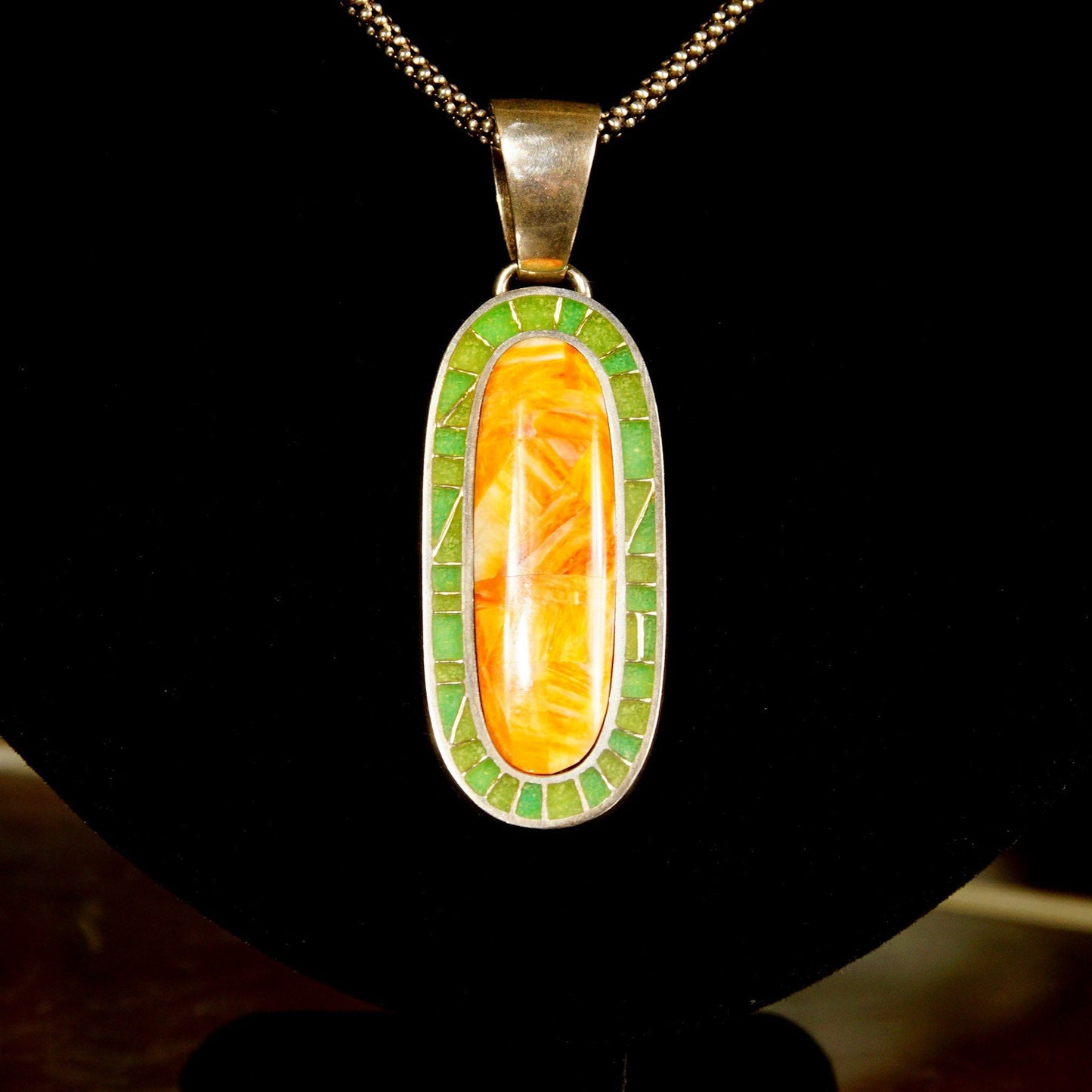 Vintage 925 sterling silver pendant necklace featuring an elongated oval design with orange carnelian agate and green aventurine mosaic inlay, measuring 1 3/8 inches in length, suspended from a large silver bail on a chain.