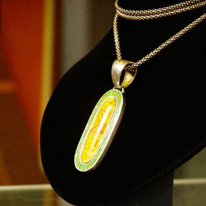 Vintage 925 sterling silver pendant necklace with mosaic orange carnelian agate and green aventurine inlay on a long oval pendant, 1 3/8 inches long, with a large silver bail, displayed on a black velvet jewelry stand.