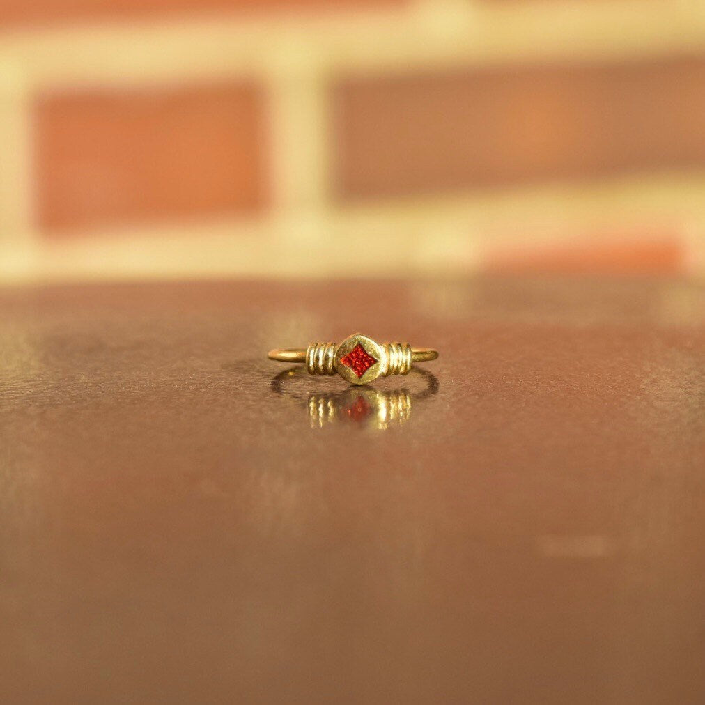 14K gold ring with red enamel starburst detail on reflective surface