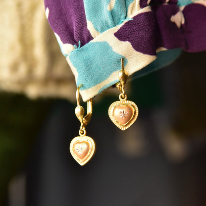 Vintage 14K yellow and rose gold heart dangle earrings with diamond-cut accents and leverback closures, hallmarked 585 and ARPAS, measuring 26mm long, shown on a colorful cloth backdrop.