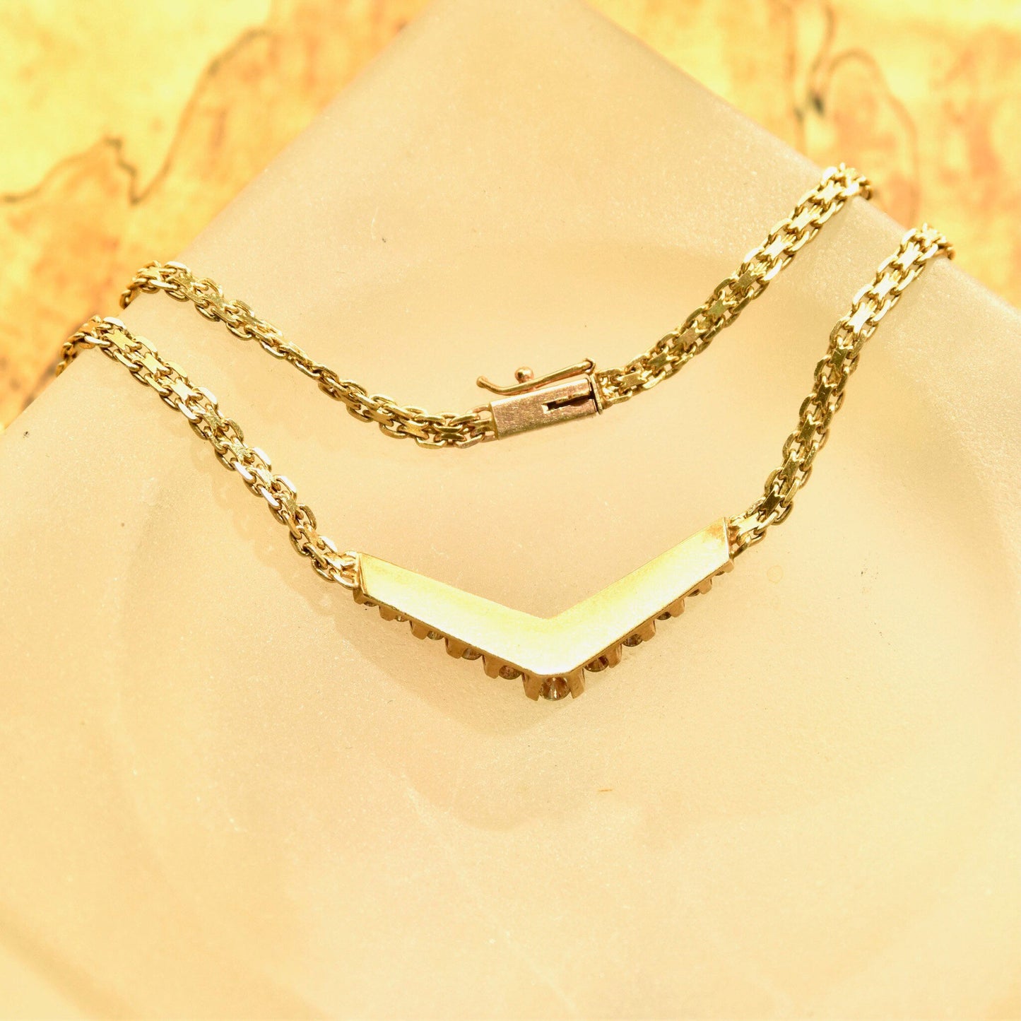 14K yellow gold chevron necklace with channel set brilliant cut diamond pendant on a delicate mesh link chain, measuring 15 1/4 inches in length, displayed on a light beige textured background.