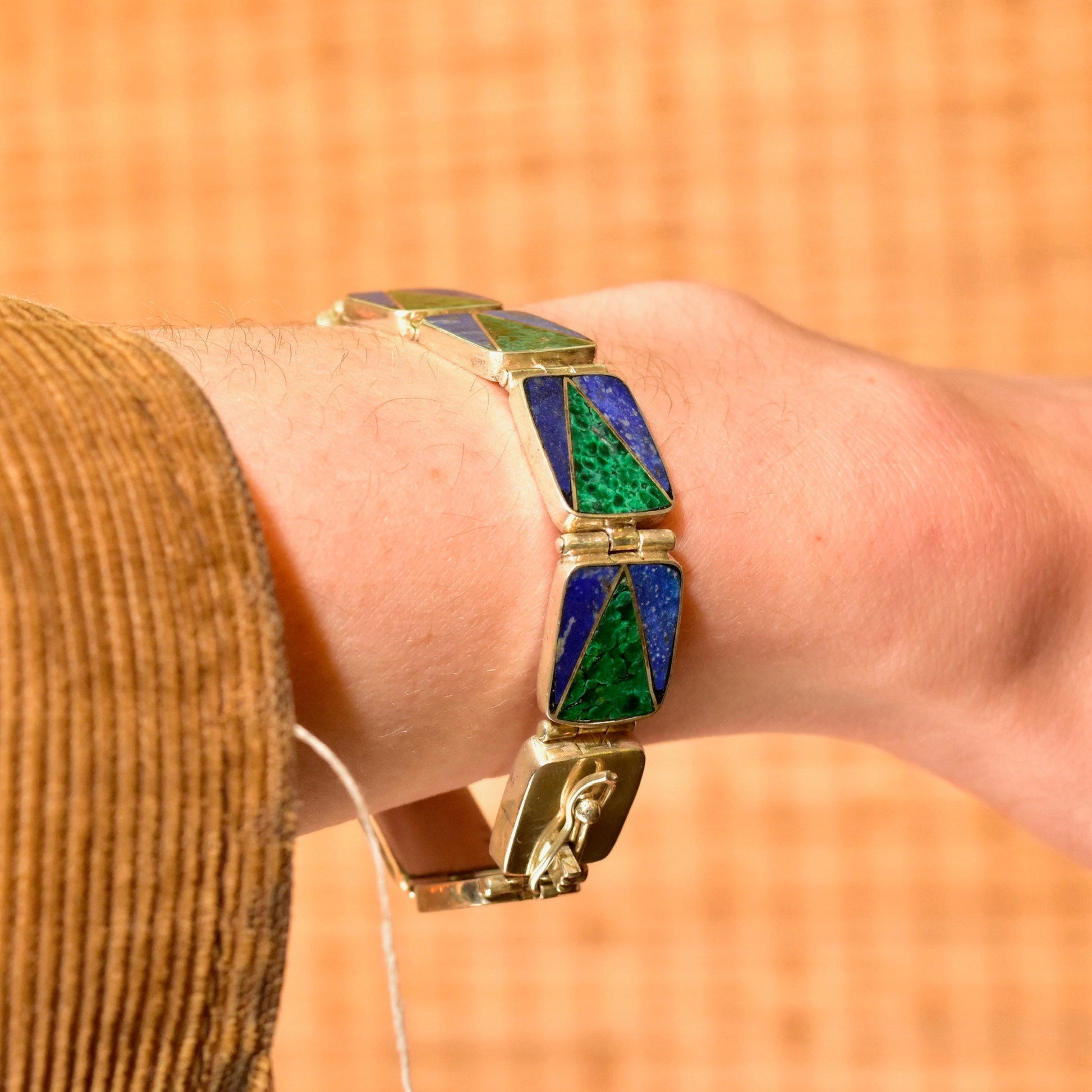 Vintage sterling silver link bracelet with geometric malachite and lapis lazuli inlay, showcasing a bohemian modernist style, worn on a wrist against an orange background.