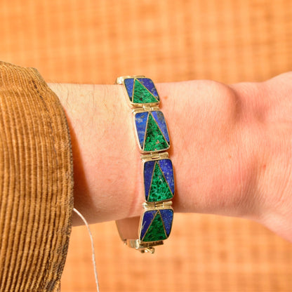 Vintage sterling silver link bracelet featuring geometric inlaid panels of vibrant green malachite and deep blue lapis lazuli stones, creating a bold bohemian modernist design. The bracelet measures 7 1/4 inches long and is shown worn on a person's wrist against a warm orange background.