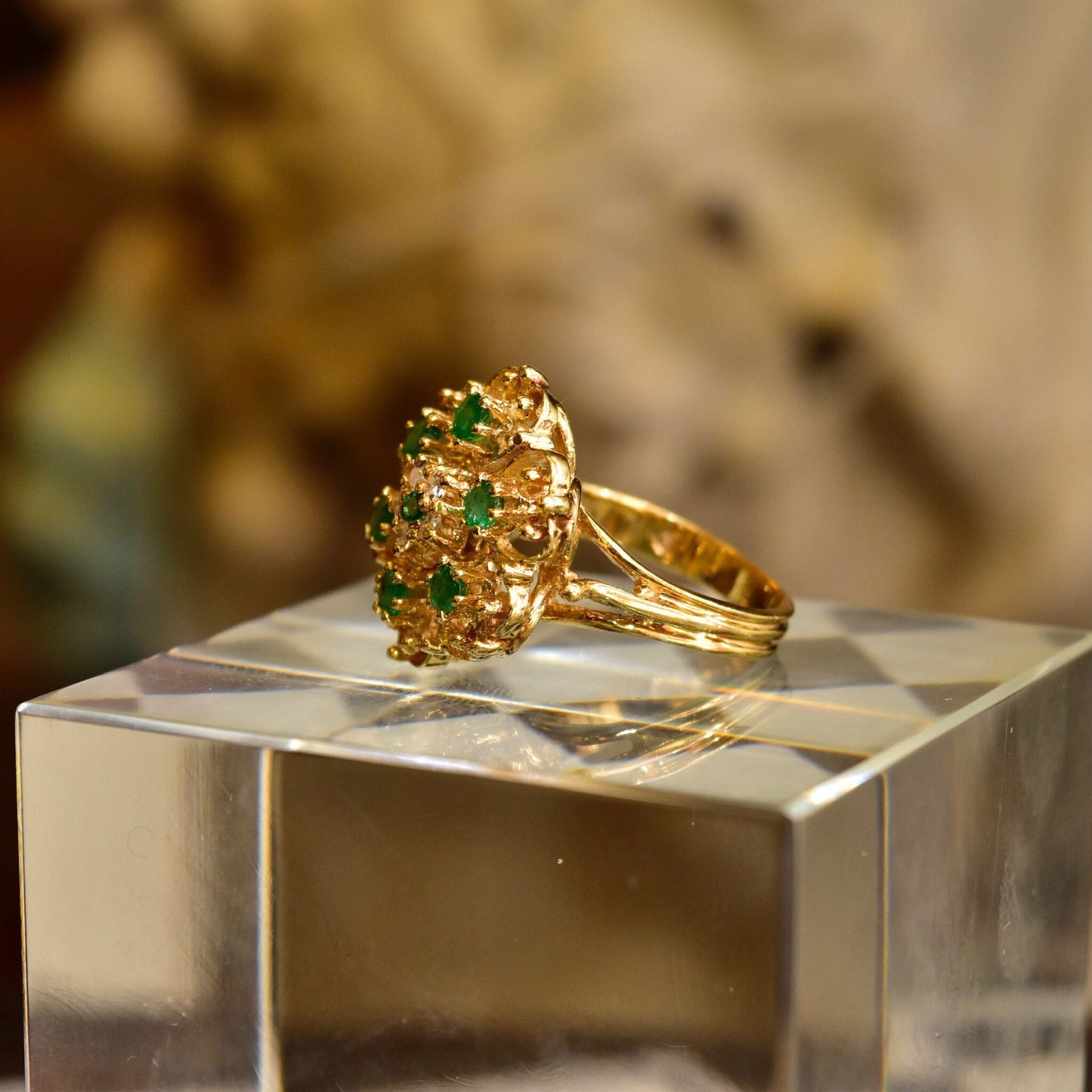 14K yellow gold emerald and diamond cluster cocktail ring featuring a dome-shaped floral design set with round emeralds surrounded by small diamonds, displayed on a reflective surface, size 7 1/2 US.