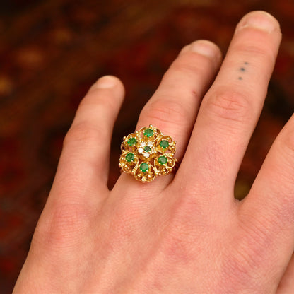 14K yellow gold emerald and diamond cluster cocktail ring on a hand, featuring a domed floral design with round green emerald center surrounded by small diamonds, worn on the ring finger, size 7 1/2 US.