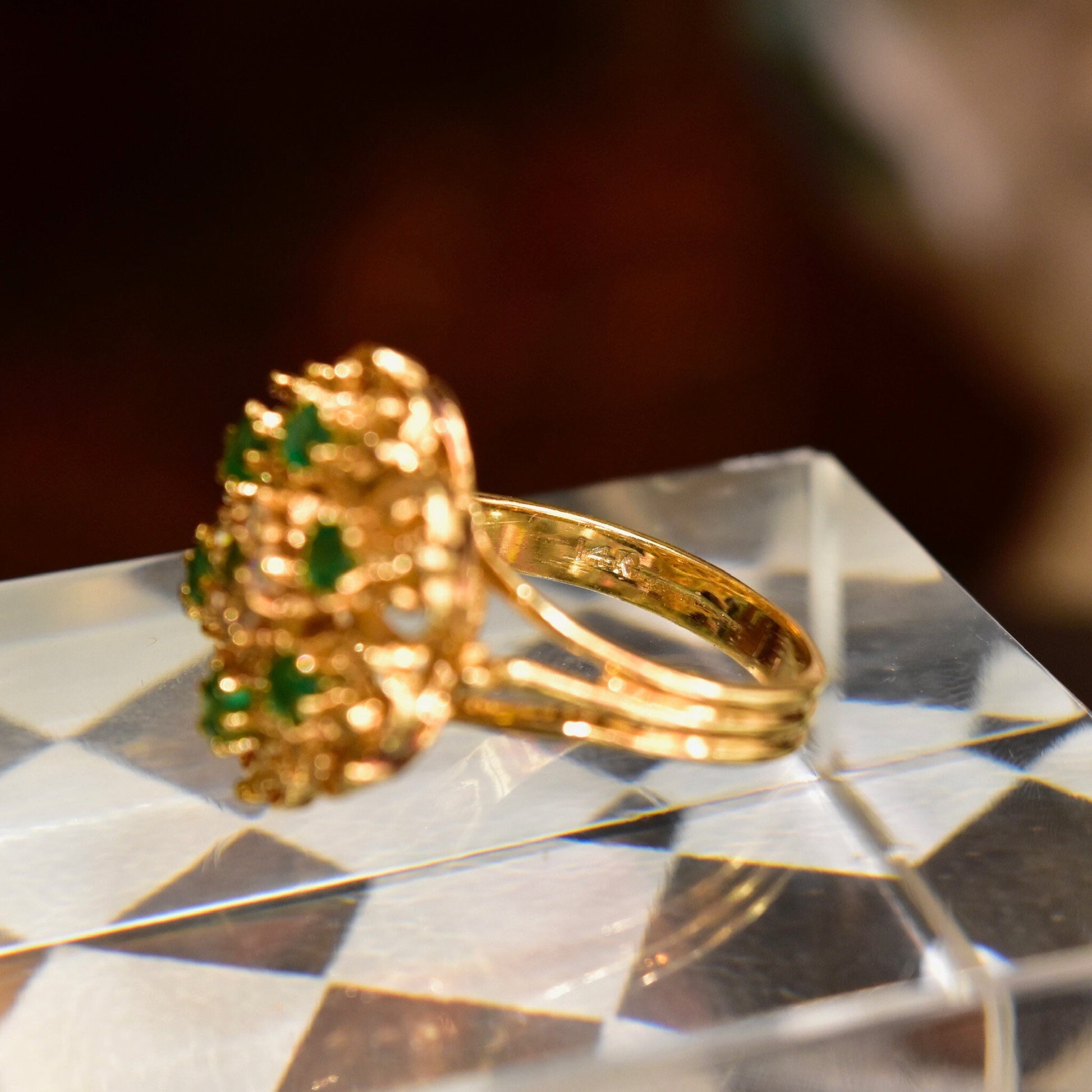 14K yellow gold emerald and diamond cluster dome cocktail ring, featuring green gemstones in a floral design, on a tiled surface, size 7 1/2 US.