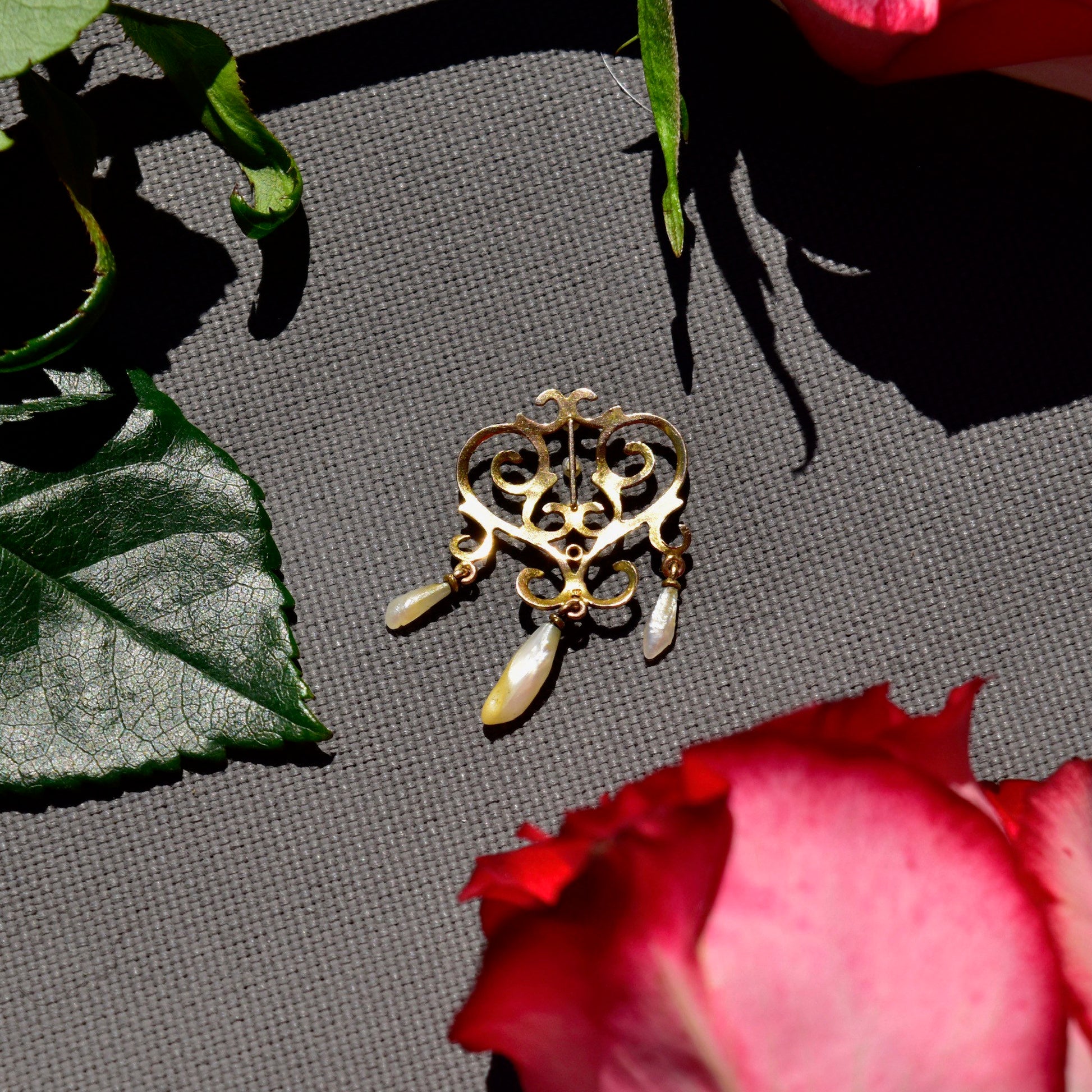 Vintage 14K yellow gold lavaliere pendant with pearl accents and tassel details in need of repair, displayed on grey backdrop with rose petal elements, measuring 33mm.