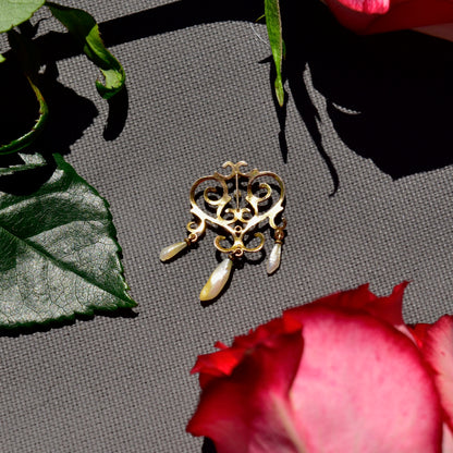 Vintage 14K yellow gold lavaliere pendant with pearl accents and tassel details in need of repair, displayed on grey backdrop with rose petal elements, measuring 33mm.