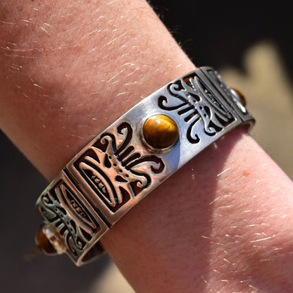 Vintage TAXCO Sterling Silver Tiger's Eye Link Bracelet with tribal motifs displayed on a wrist, featuring a heavy silver closed cuff design and a security chain clasp.