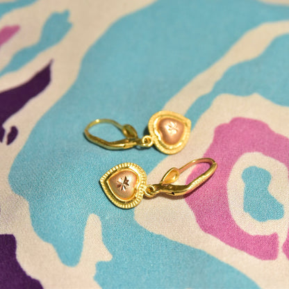 Vintage 14K yellow and rose gold heart dangle earrings with diamond-cut accents and leverback closures on colorful fabric background