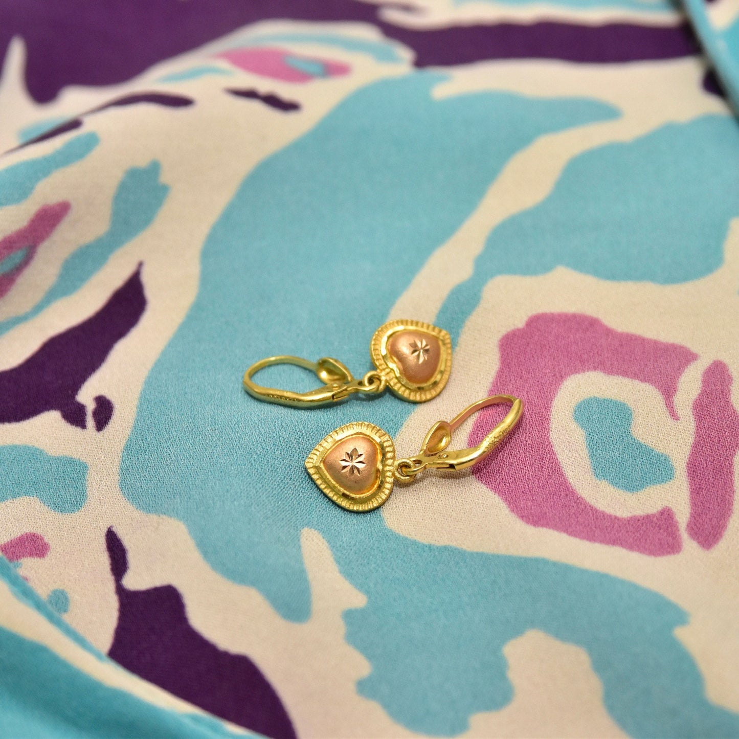 Vintage 14K yellow and rose gold heart dangle earrings with diamond-cut accents and leverback closures, hallmarked 585 and ARPAS, measuring 26mm in length, shown on a colorful patterned fabric background.