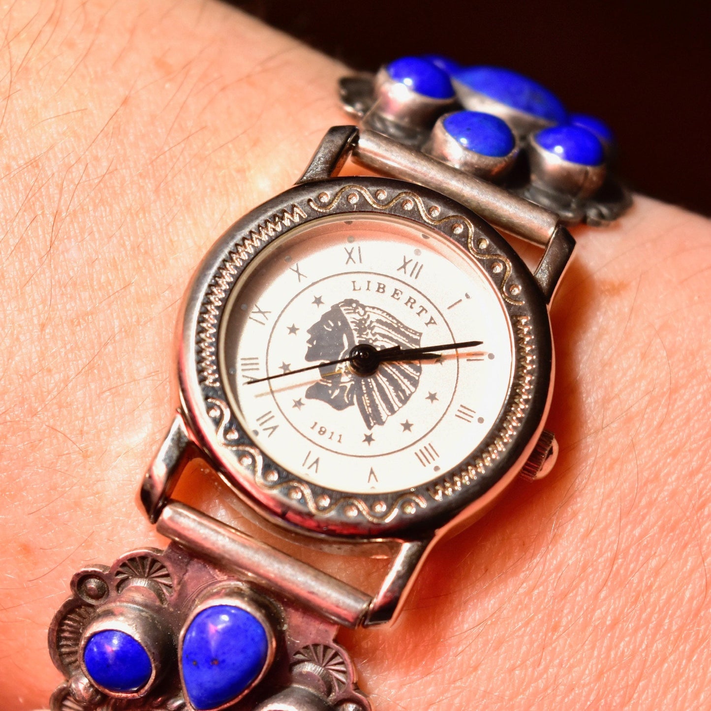 Vintage Liberty 1911 Navajo A. Cadman sterling silver and lapis lazuli ladies wrist watch with adjustable bracelet, featuring an engraved silver case and blue lapis lazuli cabochons on the bracelet. The face displays Roman numerals and an ornate silver design surrounding the quartz automatic movement.