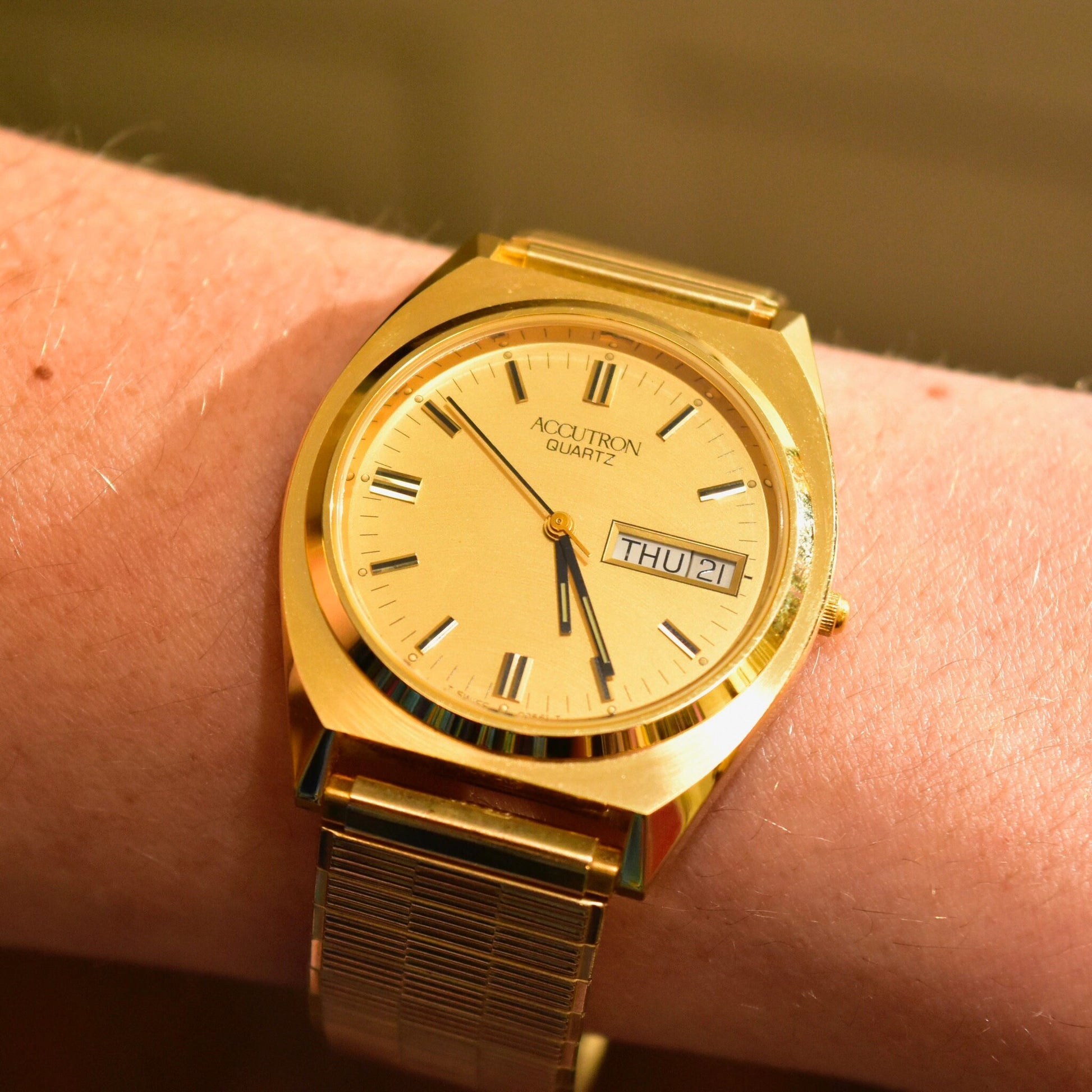 Vintage 1988 Bulova Accutron gold tone watch with day and date display, housed in original box with papers, shown on wrist with two-tone expandable bracelet.