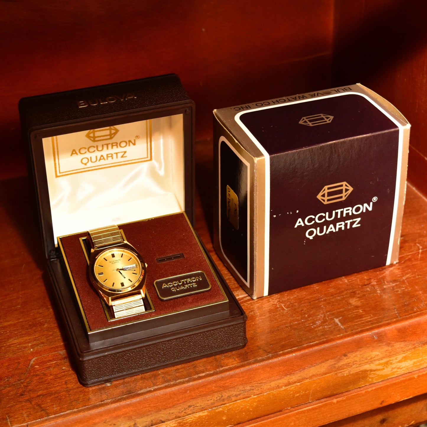 Vintage 1988 Bulova Accutron gold tone Swiss quartz wristwatch with day/date function, original box and papers, displayed on wooden surface.