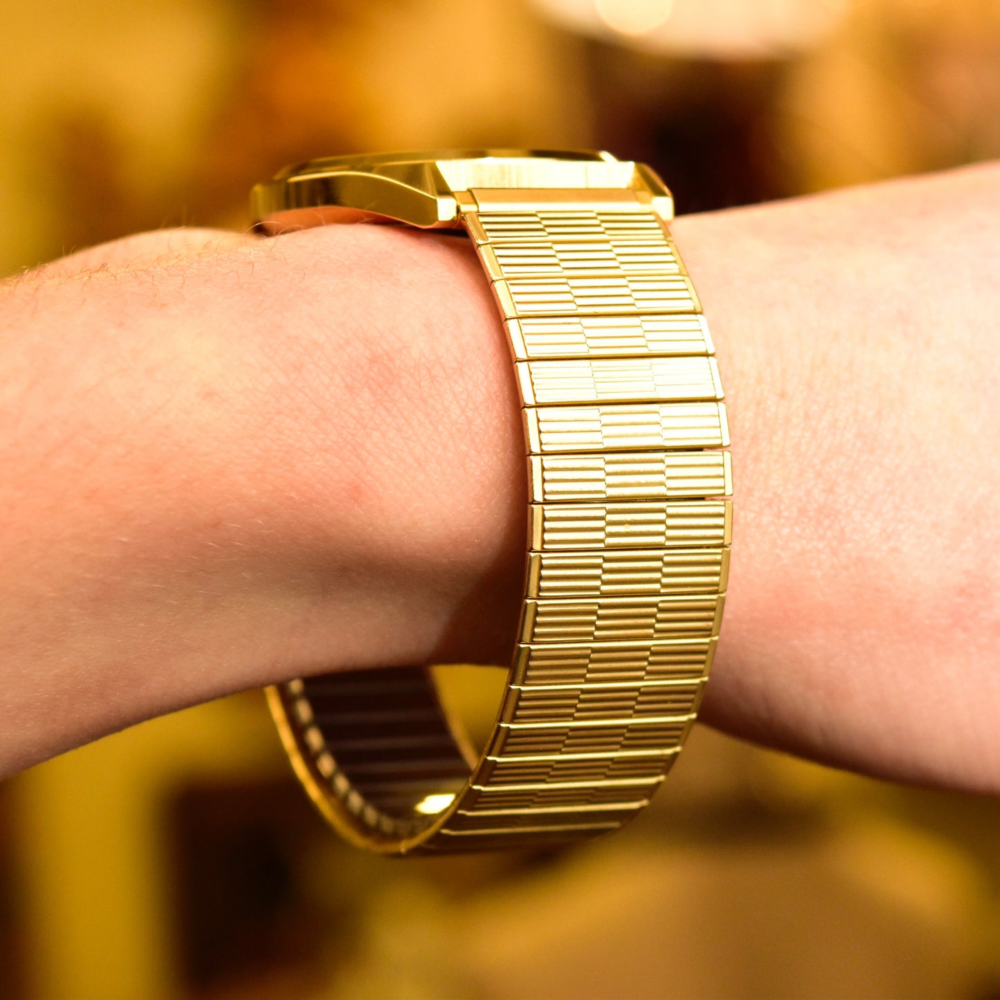 Vintage 1988 Bulova Accutron gold tone Swiss quartz wristwatch with day/date feature and two-tone stretch band, shown on a person's wrist against a blurred golden background.