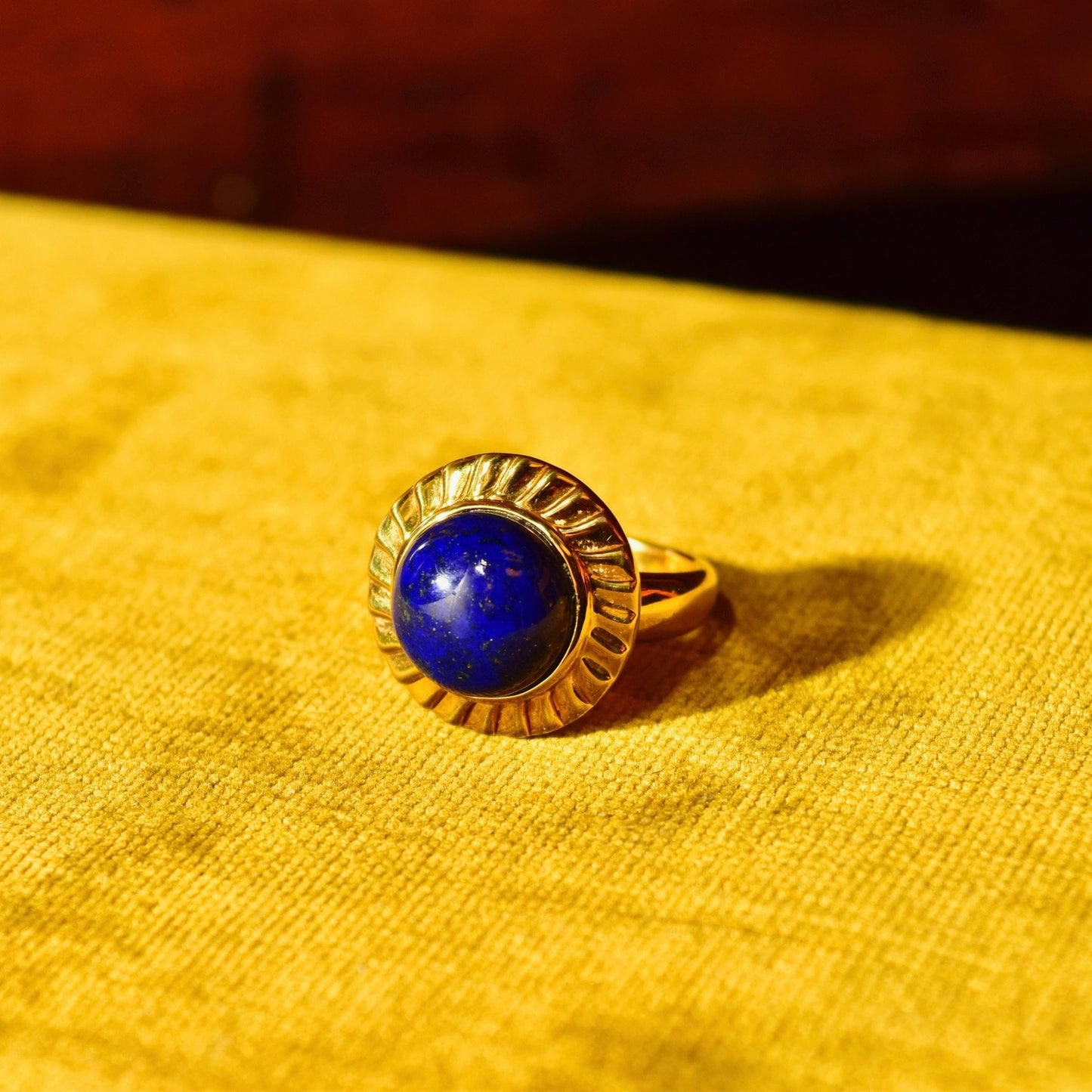 14K yellow gold ring with round blue lapis lazuli cabochon gemstone, cocktail solitaire style, size 7.5 US, against mustard yellow fabric background