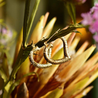 14K yellow gold textured heart hoop earrings on a green and pink floral background