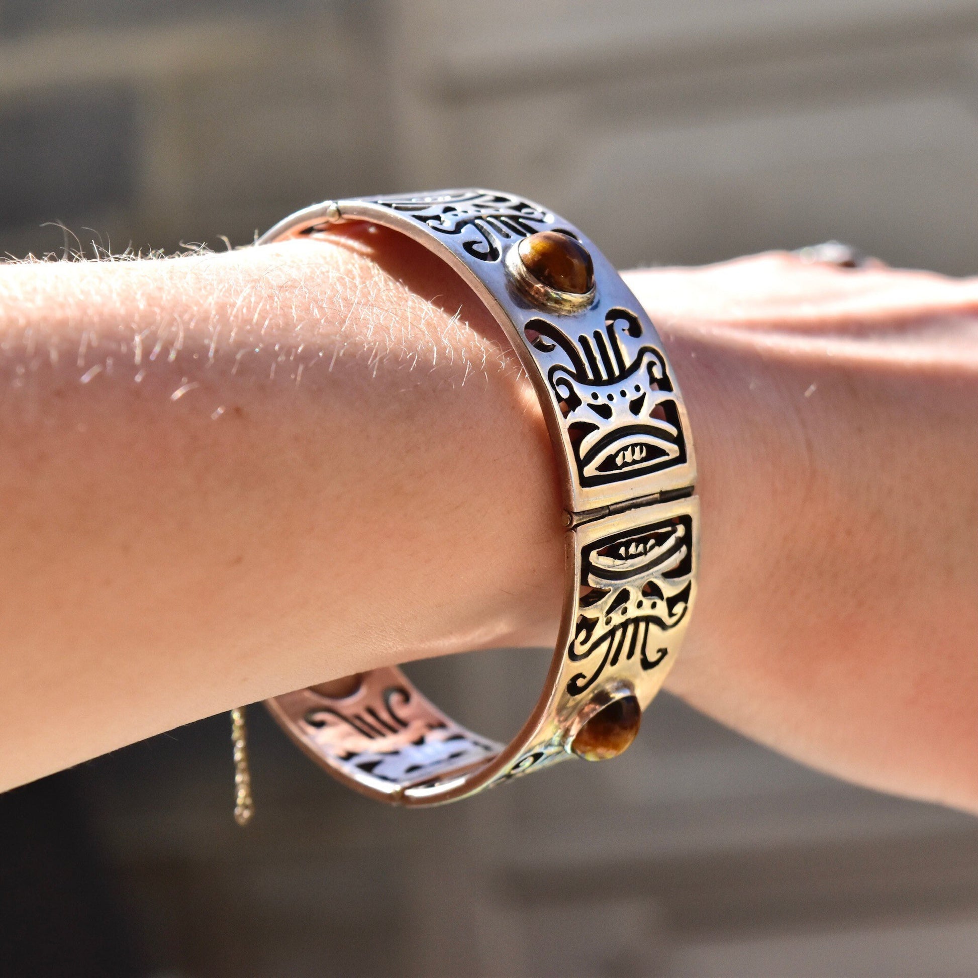 Vintage TAXCO Sterling Silver Tiger's Eye Link Bracelet with tribal motifs on a person's wrist, featuring a heavy silver closed cuff/bangle design and a security chain clasp.