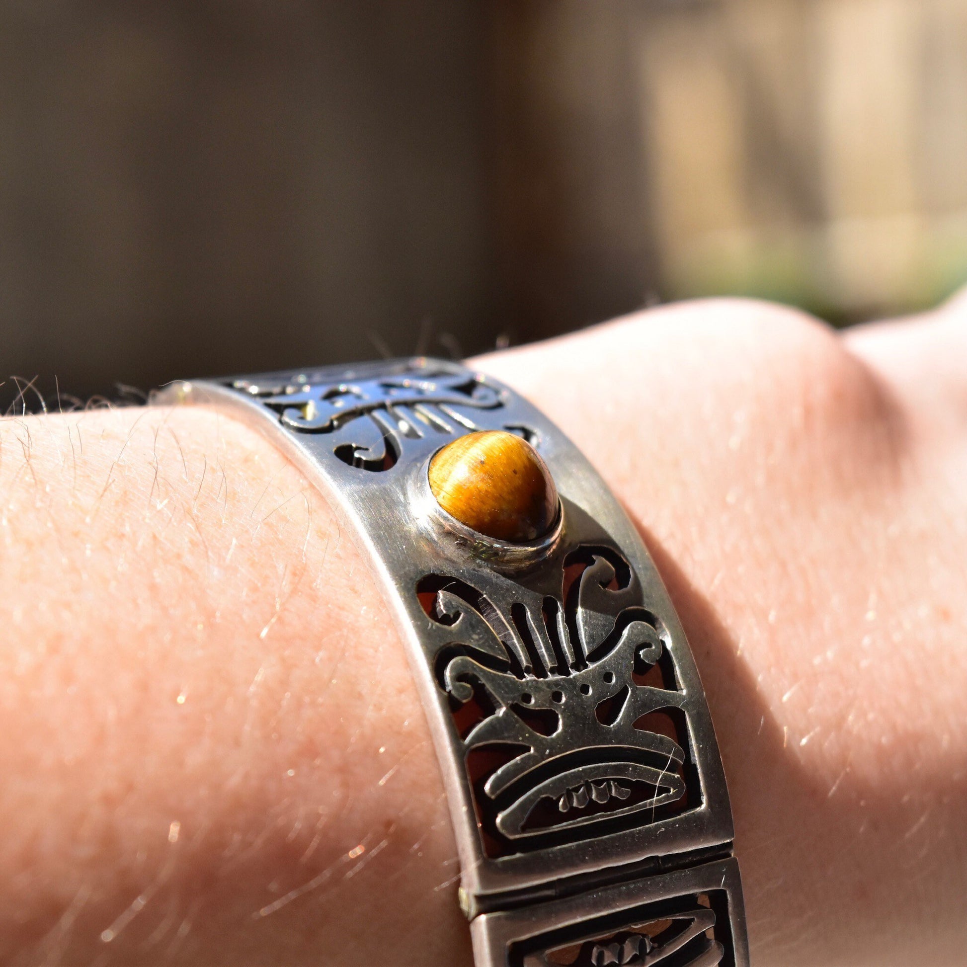 Vintage TAXCO sterling silver tiger's eye link bracelet featuring tribal motifs on a person's wrist, with a heavy silver closed cuff design and security chain clasp.