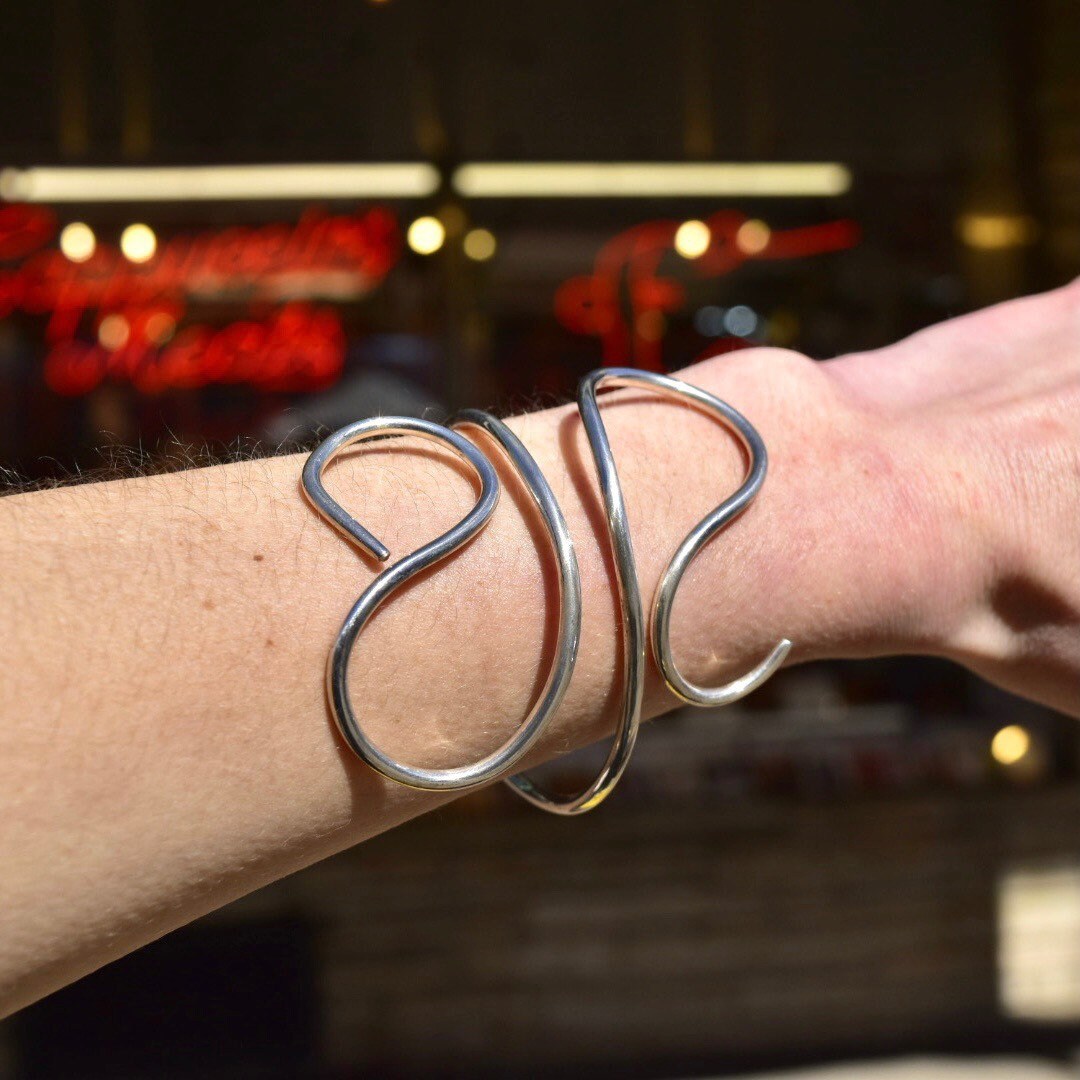 Vintage MMA Sterling Silver Wire Wrap Cuff Bracelet on wrist with minimalist solid silver swirl design, adjustable to 7 1/2 inches, against blurred background of red lights